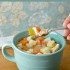 A mug with chicken soup in it, and a spoon with chicken soup on it.