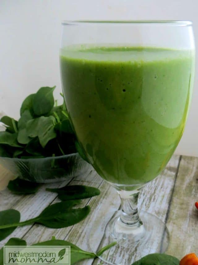Pineapple Almond Milk Smoothie in a cup with spinach leaves in the background.