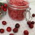 A glass jar of cranberry sugar scrub on a white and red background.