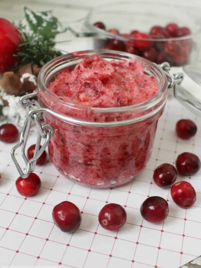 Cranberry sugar scrub in a glass jar with whole cranberries outside the base of the jar.