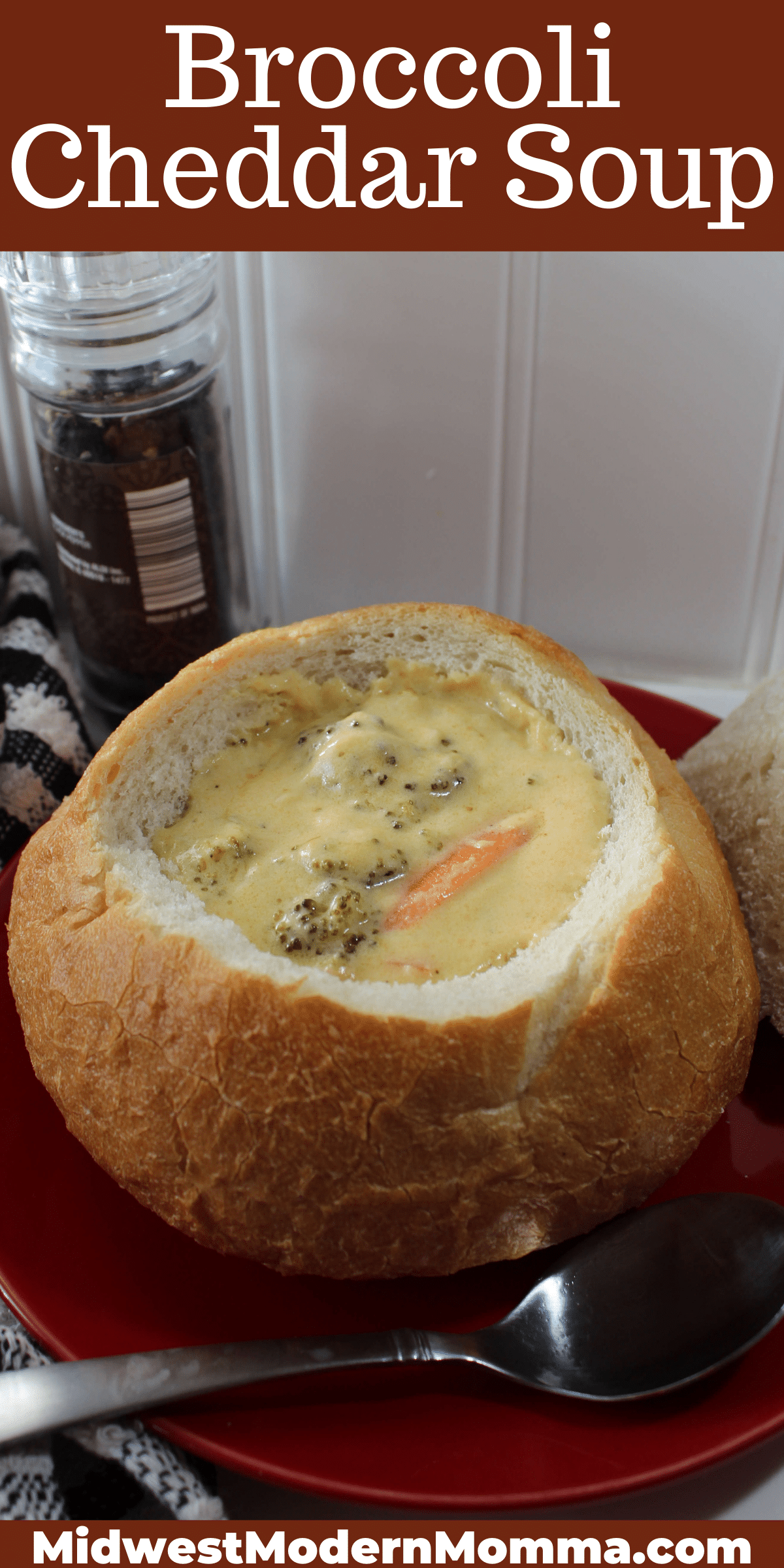 A bread bowl full of broccoli cheddar cheese soup on a red plate with a spoon next to it.