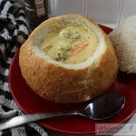 Copycat Panera Broccoli Cheddar Cheese Soup in a bread bowl on a red plate.