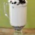 White hot chocolate in a glass mug topped with whipped cream and crumbled cookie pieces.