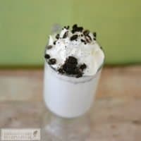 White hot chocolate in a glass mug topped with whipped cream and crumbled cookie pieces.