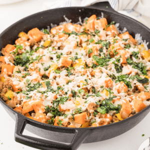 Cumin-infused turkey and sweet potato in a cast iron skillet with melted cheese on top.