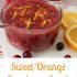 Cranberry sugar scrub in a glass jar with orange zest on the top with text saying "Sweet Orange Cranberry Scrub".