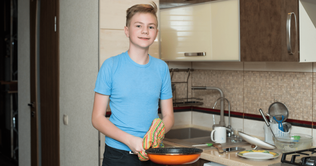 Boy wearing a blue shirt, holding a skillet  with a hot pad holder.
