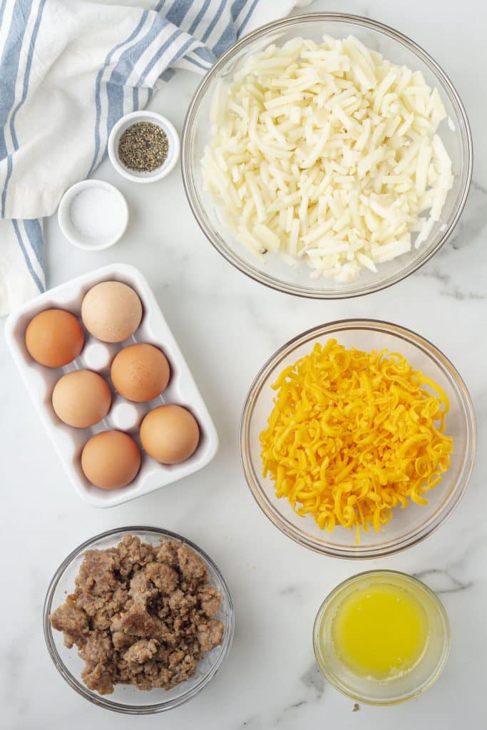 Ingredients for sausage egg muffins in various size containers: hash browns, shredded cheese, butter, sausage, eggs, salt, and pepper.