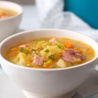 A bowl of lentil soup with chunks of potato, carrot, and ham visible.