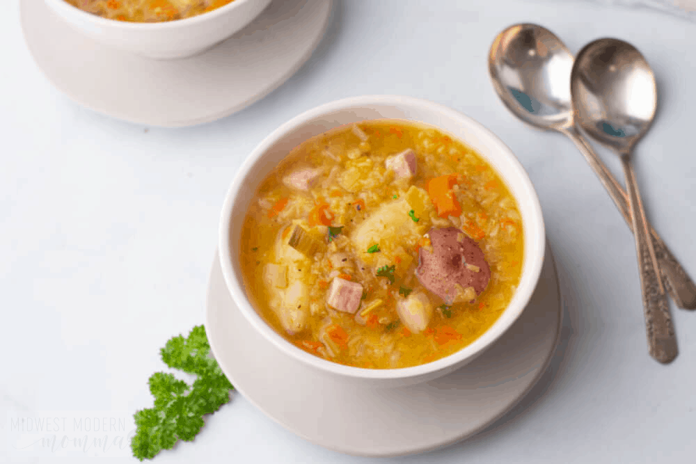 Two bowls of lentil soup with ham, potato, and carrot with two soup spoons.