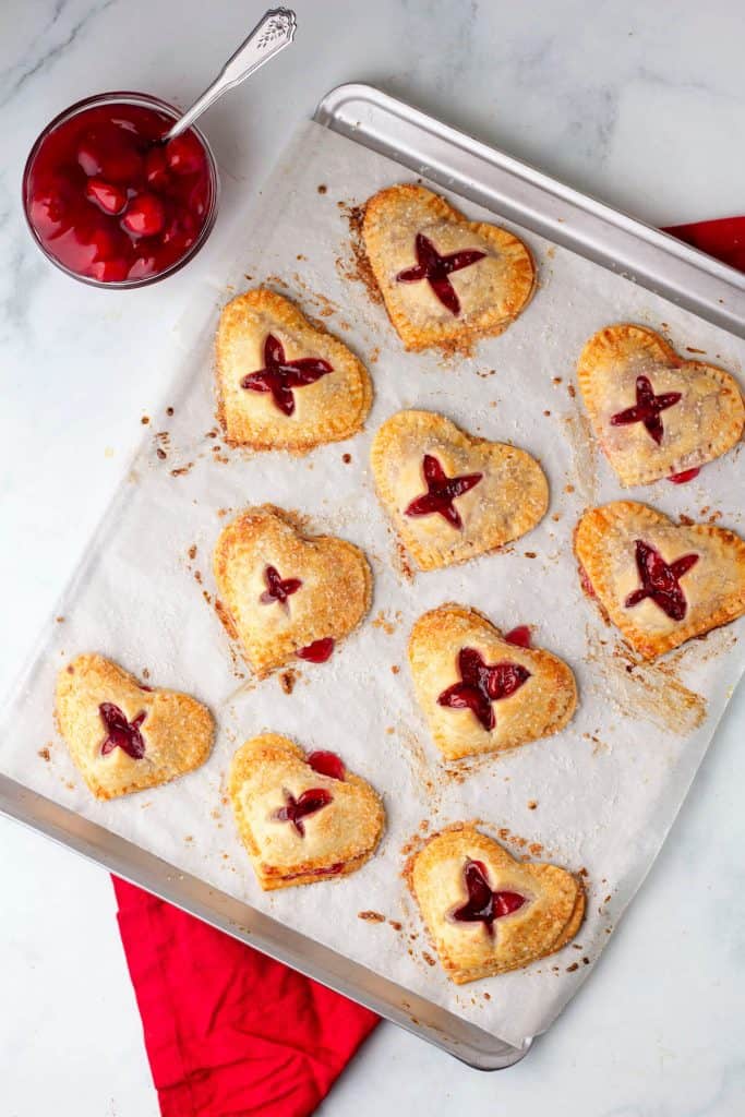 Mini cherry pies on a baking tray with a small pie of cherry pie filling