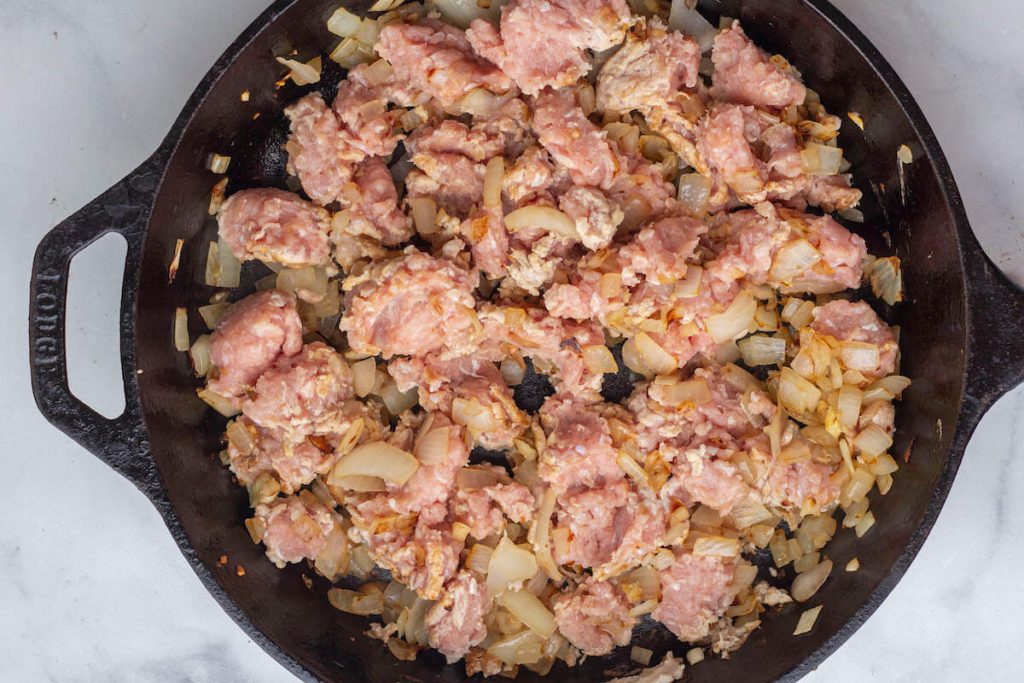Ground turkey being cooked with sauteed onions and garlic in a cast iron skillet.
