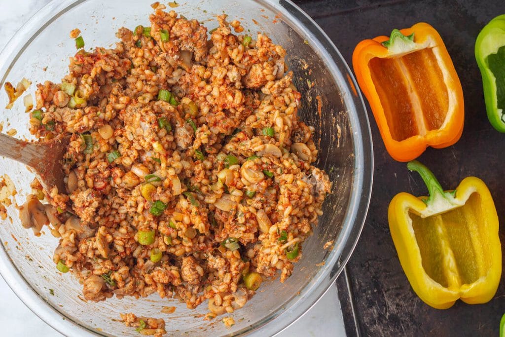 Bowl of ground turkey and barley stuffing next to a sheet of bell peppers sliced in half.