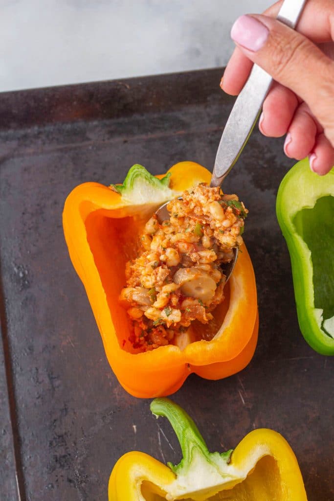 Ground turkey and barley mixture being spooned into an orange bell pepper.