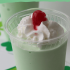 A homemade shamrock shake in a plastic cup with whipped cream and a cherry on top.