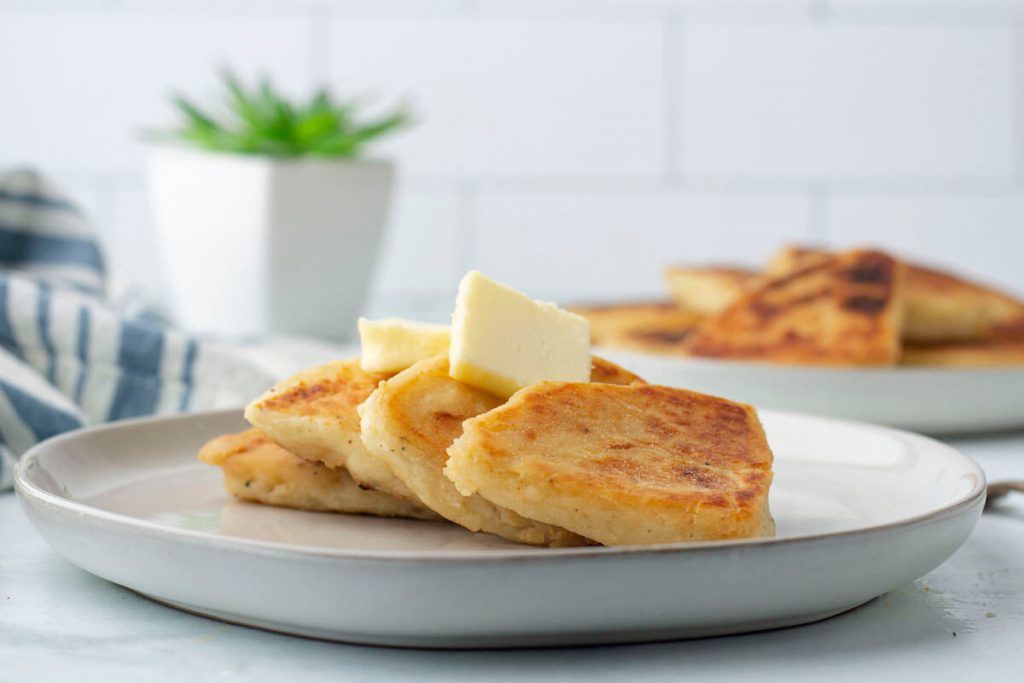 White plate of tattie scones with butter on top.