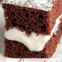 Closeup view of creamy marshmallow filling between two slices of devils food cake, with text naming the recipe a copycat Hostess Suzy Q.