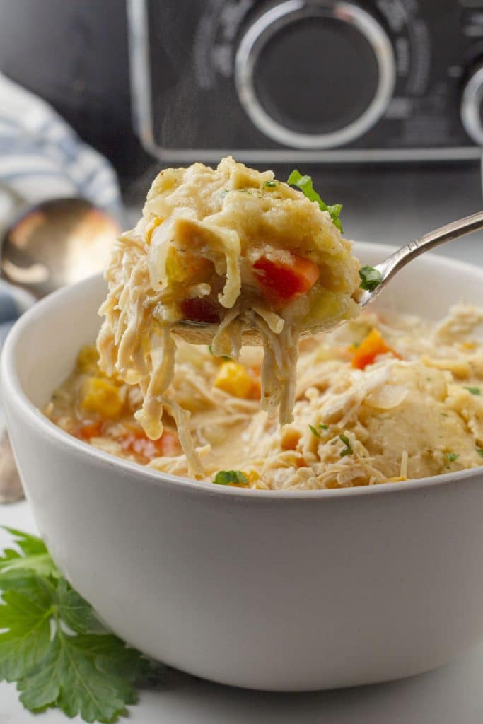 A spoonful of crockpot chicken and dumplings held above a full bowl of this delicious comfort food.