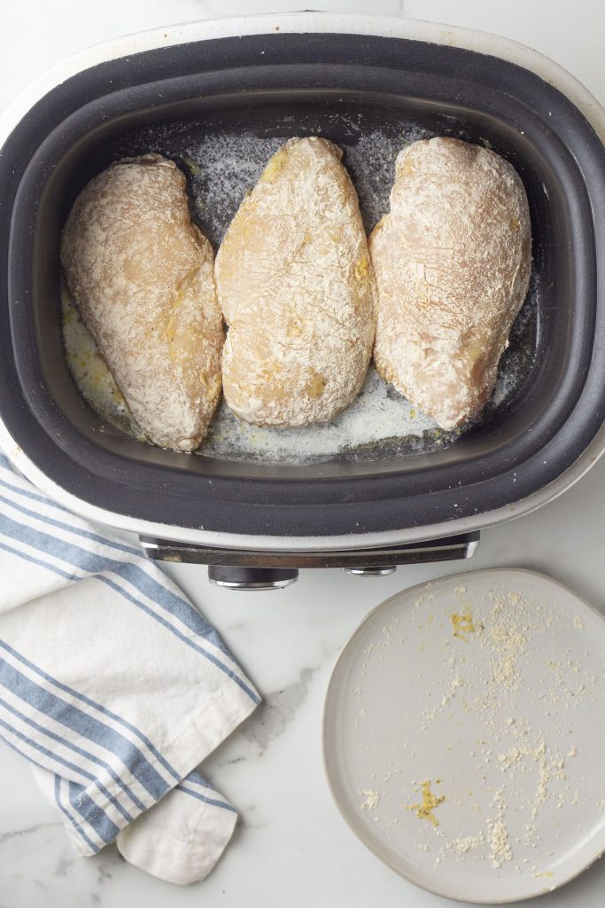 Chicken breasts browning in a slow cooker for a crockpot chicken and dumplings recipe.
