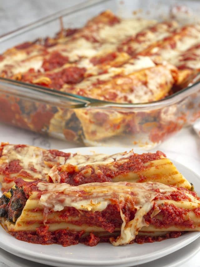Stuffed manicotti on a plate in front of a baking dish with more manicotti.