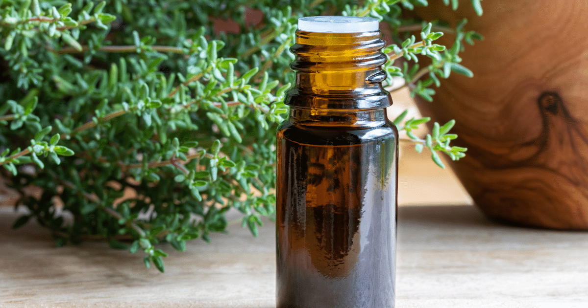 Amber essential oil bottle on wooden surface in front of thyme sprigs.