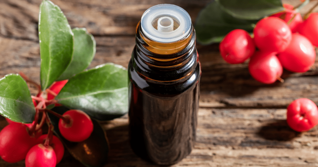 Amber essential oil bottle next to wintergreen berries.