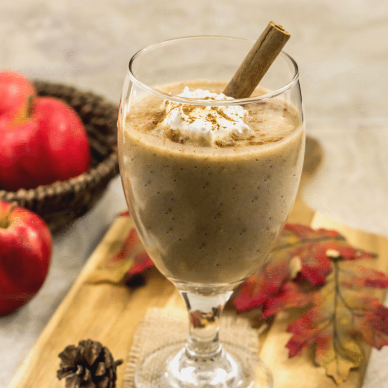 A glass of apple pie smoothie with whipped cream and a cinnamon stick.