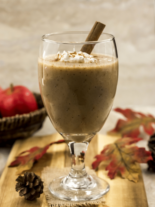 A glass of apple pie smoothie with whipped cream and a cinnamon stick.