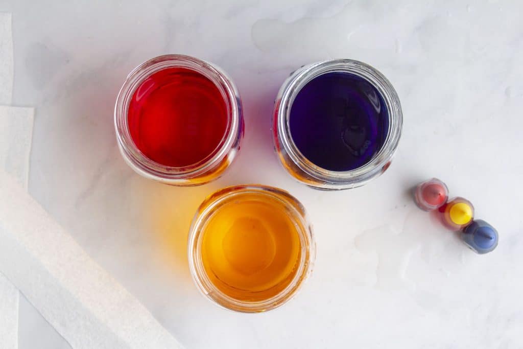 A photograph of 3 mason jars filled with colored water for the walking water rainbow experiment.