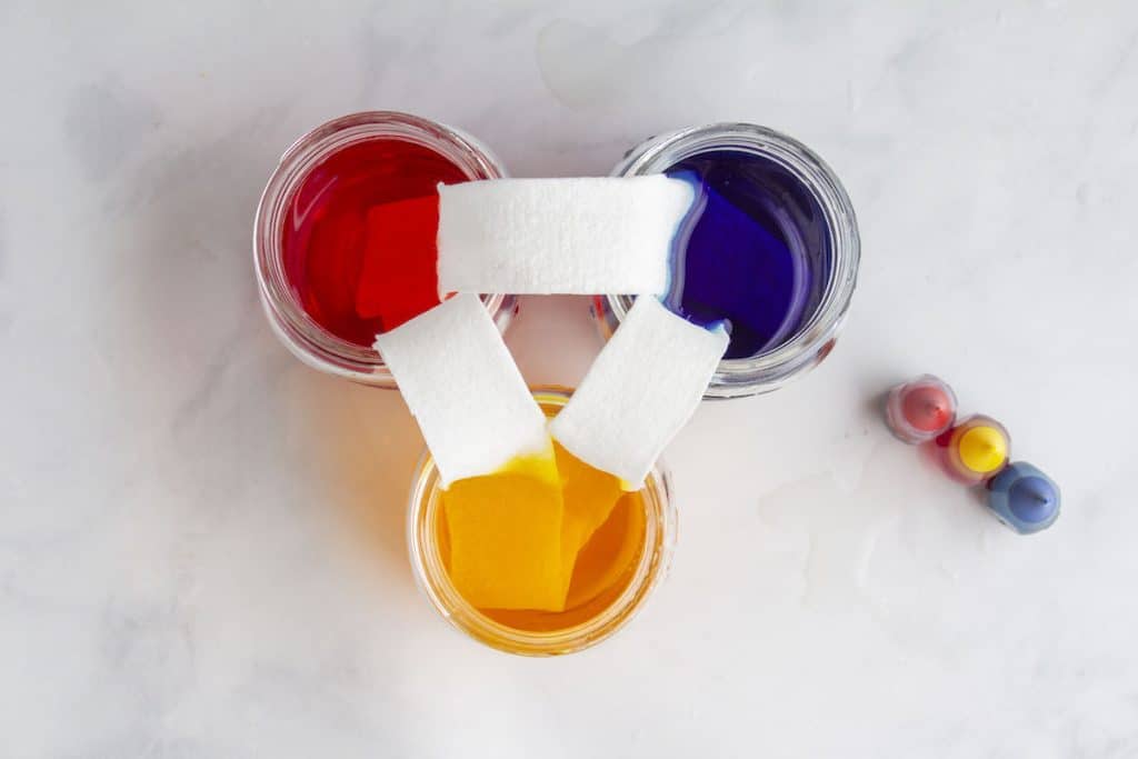 A photograph of water moving through paper towels and creating a colorful display in three glass jars.