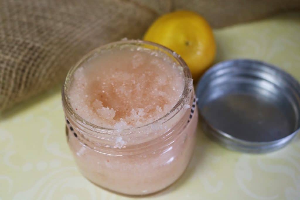 Homemade body scrub recipe in a glass jar with a lemon next to it.