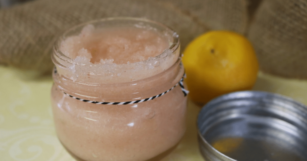 Grapefruit sugar scrub in a glass jar with a black and white string around the jar and a lmeon in the background.