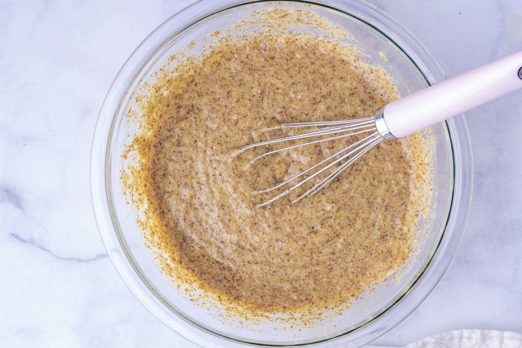 A whisk in a bowl of mixed ingredients for grain-free cornbread.