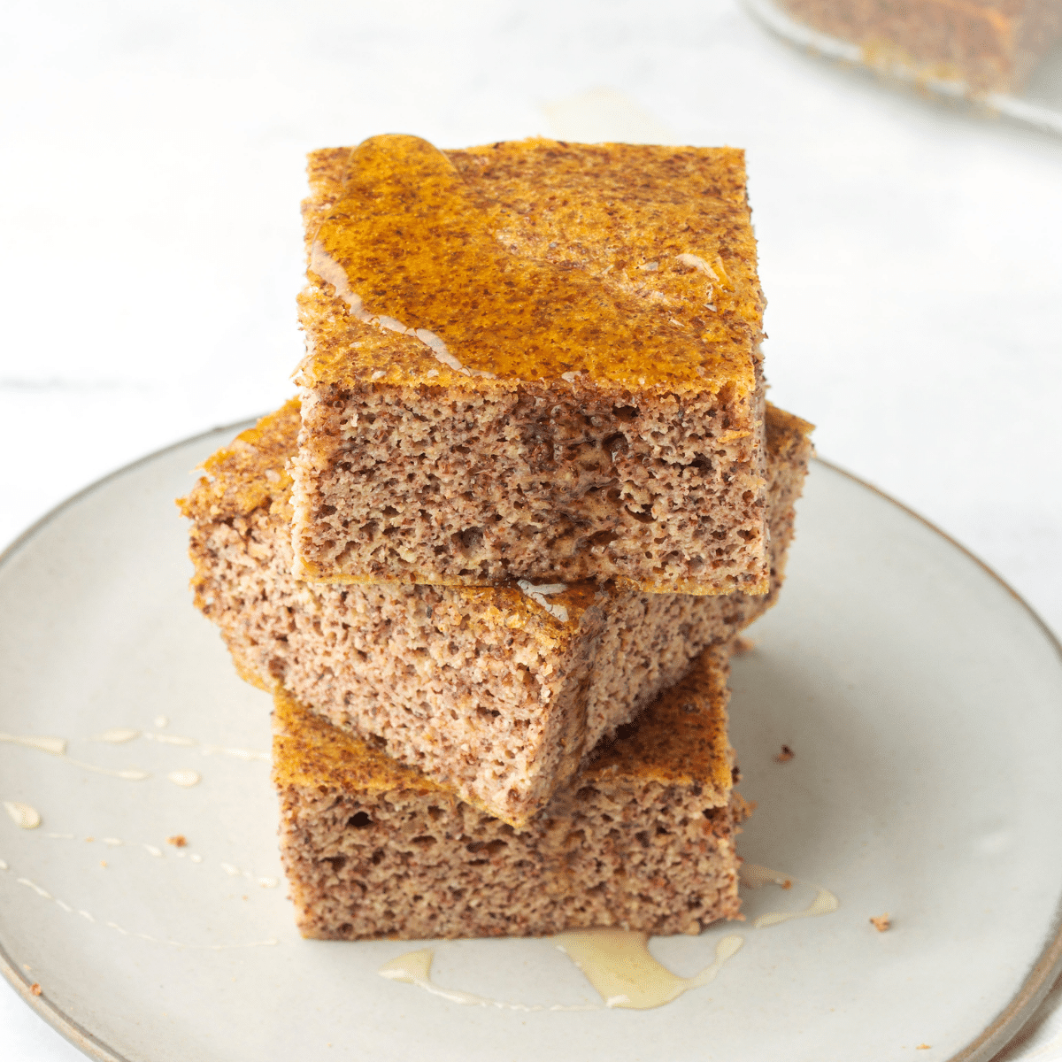 An overhead view of 3 slices of cornbread stacked on a light coloured plate with honey dripping down onto the plate from the top.