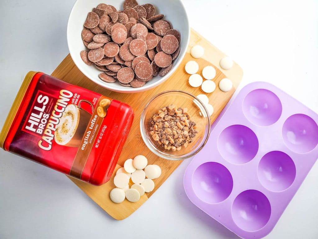 Ingredients for making English toffee cappuccino bombs laid out on a wooden board next to a purple silicone bomb mold.