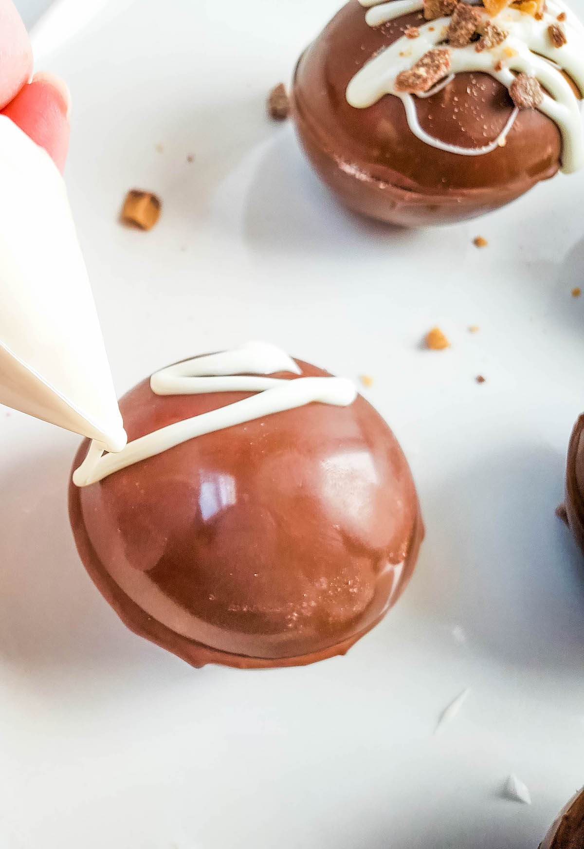 A piping bag is used to add melted white chocolate to the top of a chocolate cappuccino bomb.