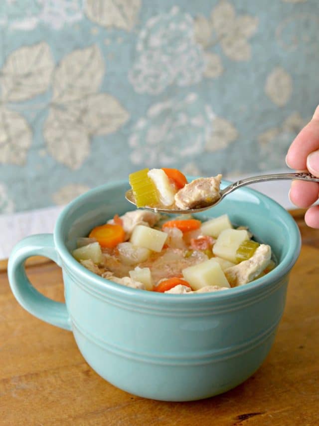 A blue mug with chicken soup, and a spoon with more soup on it.