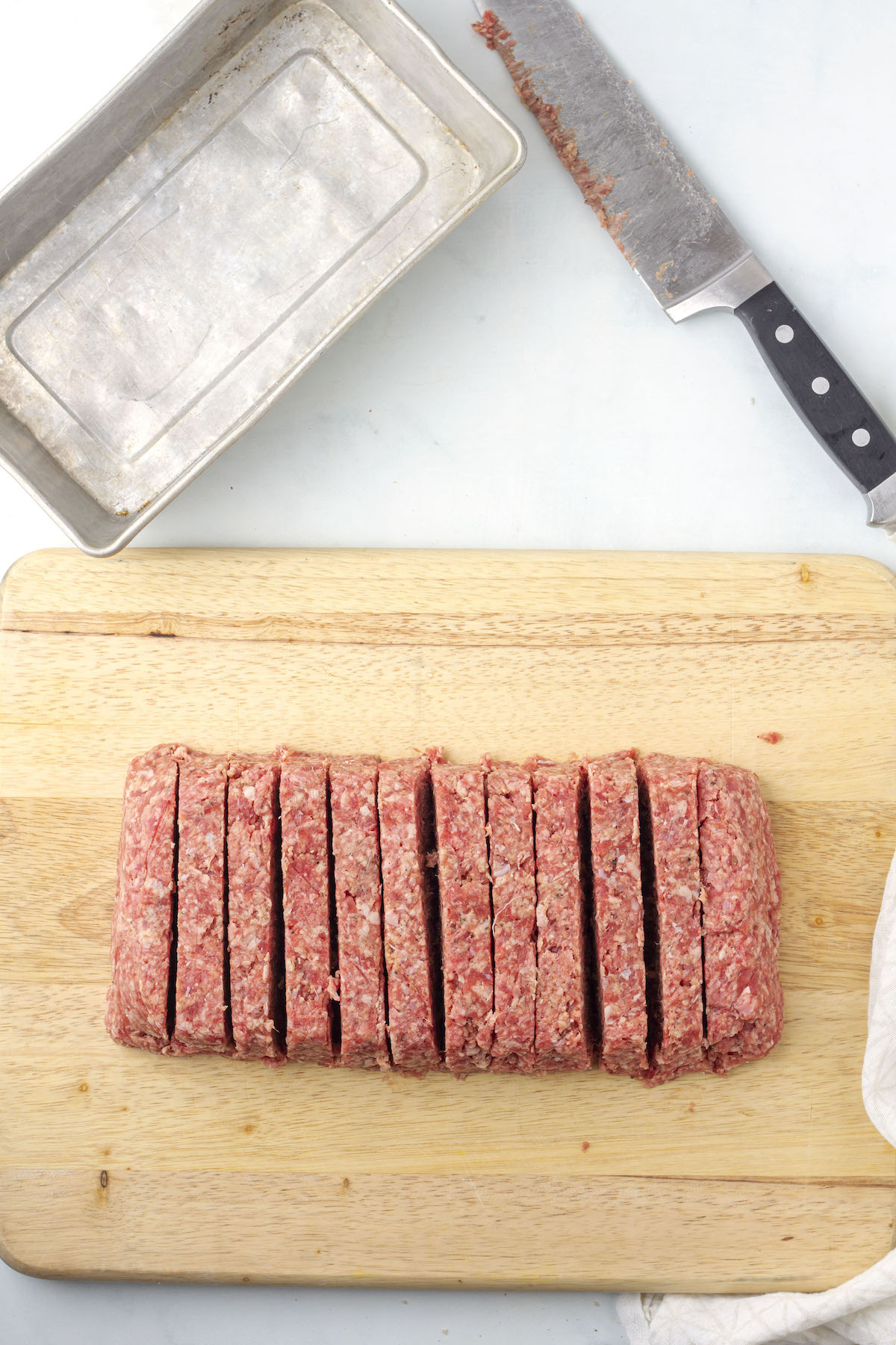 Raw square sausage mixture shaped in a log and then sliced on a cutting board.