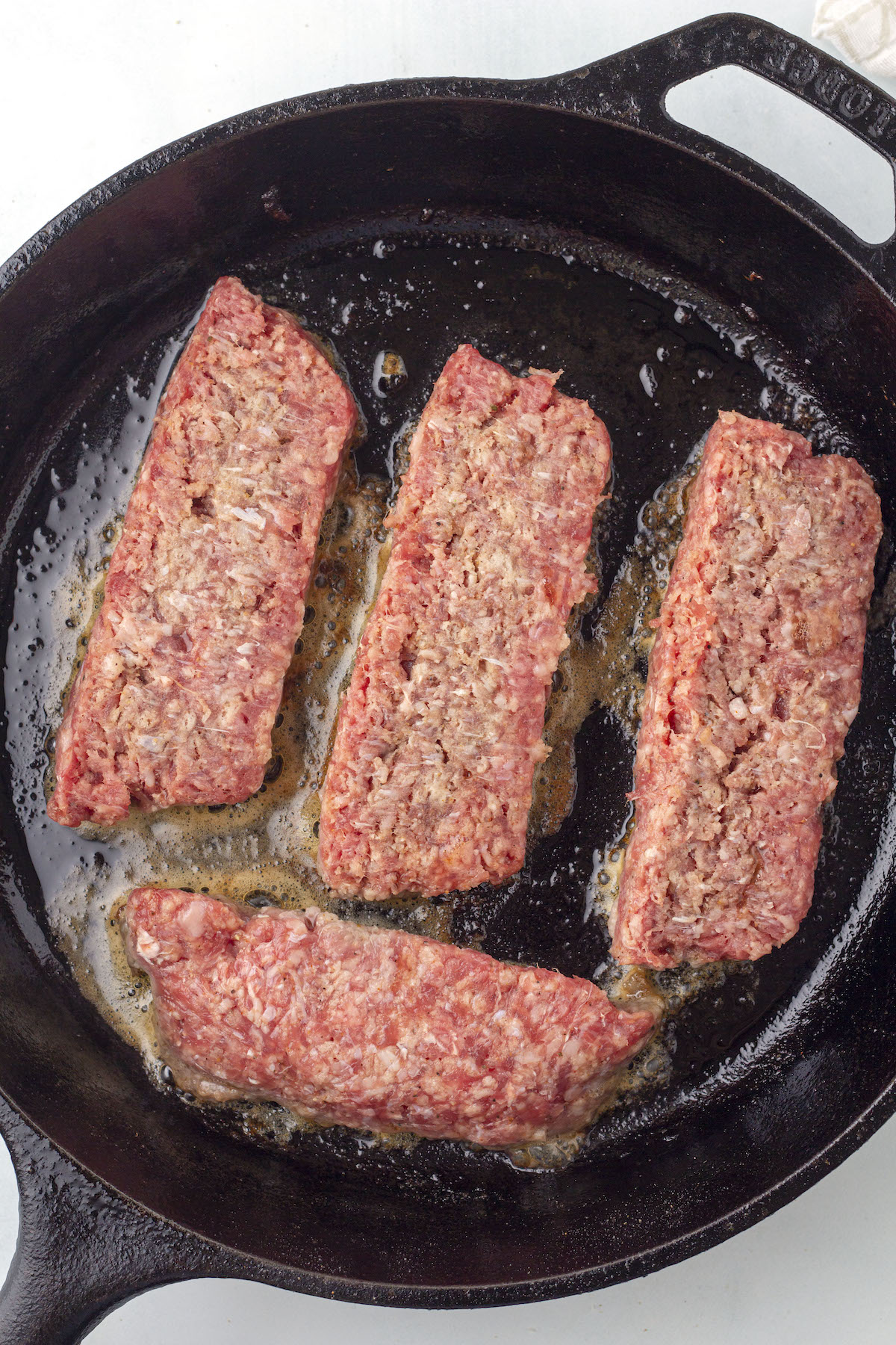 Slices of Lorne sausage being fried in a cast iron skillet.