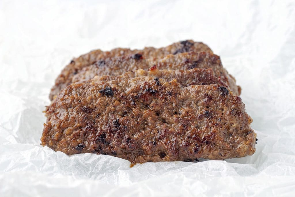 Fried square sausage patties on a layer of greaseproof or parchment paper.