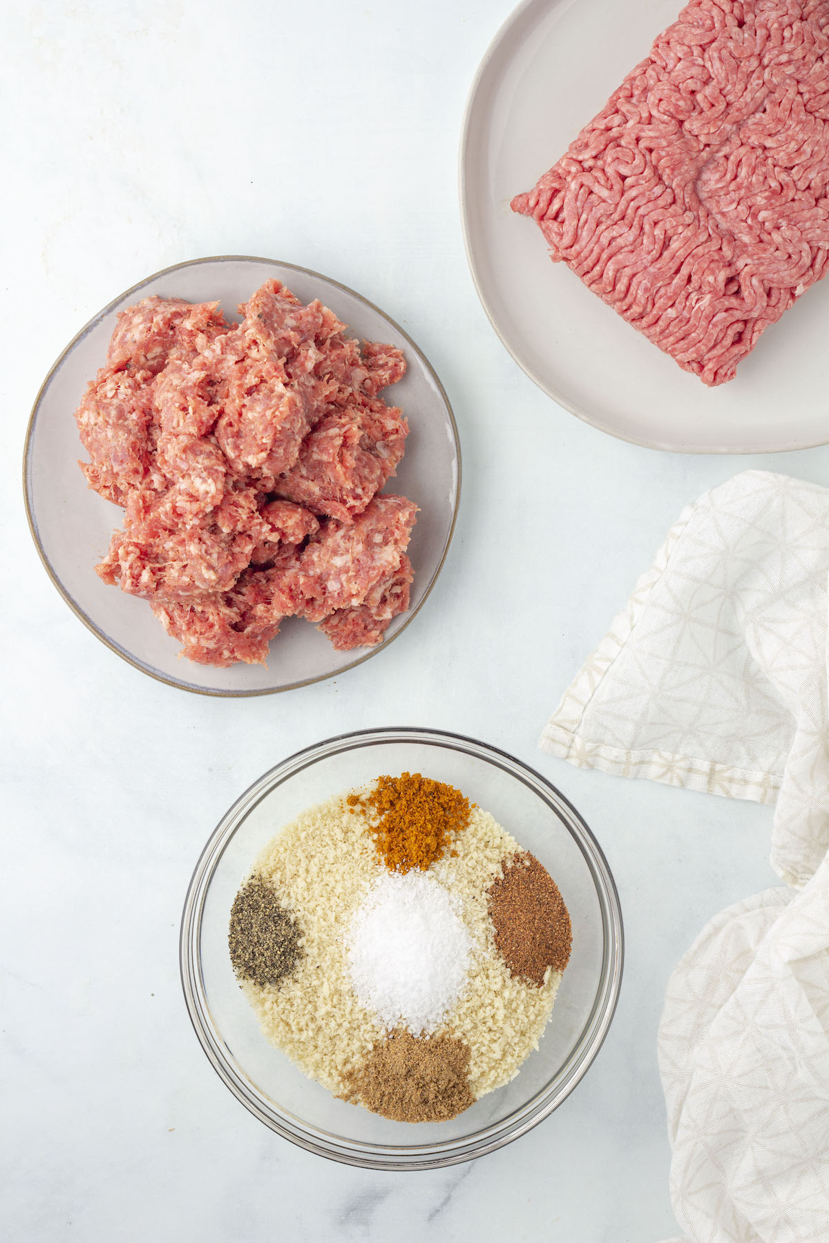 2 containers of ground meat next to a bowl of breadcrumbs with spices in a bowl.