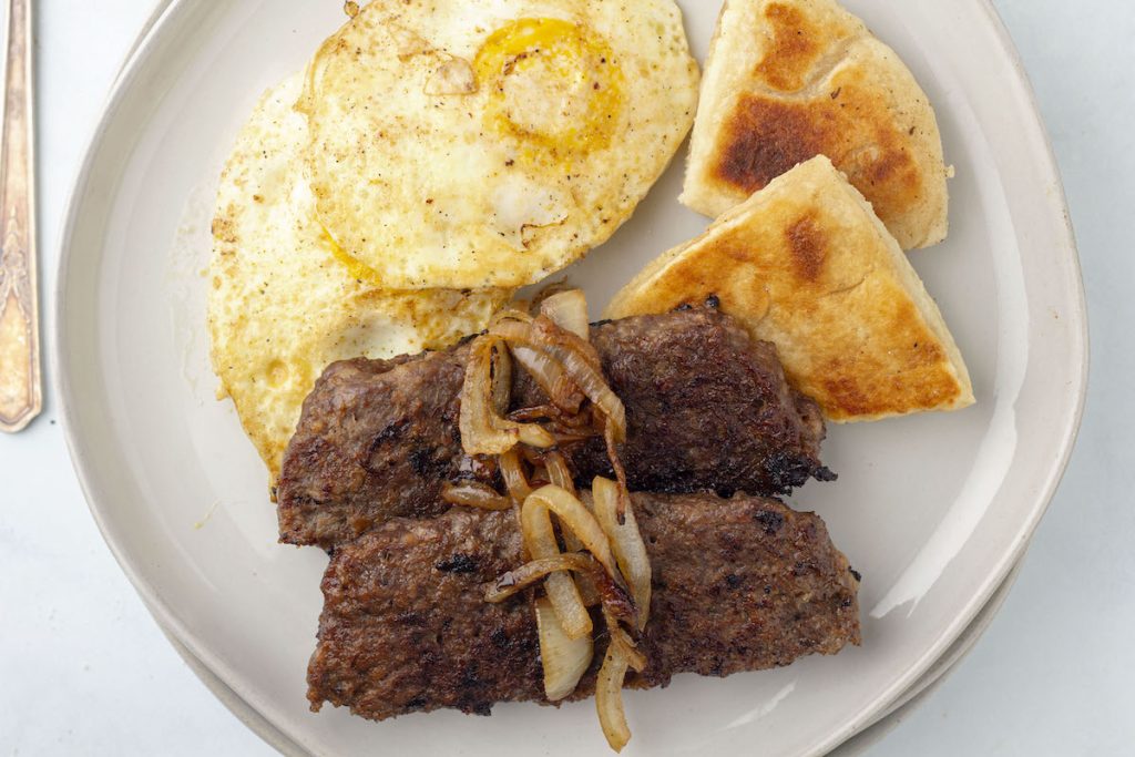 2 slices of lorne sausage on a plate with fried onions, eggs, and tattie scones.