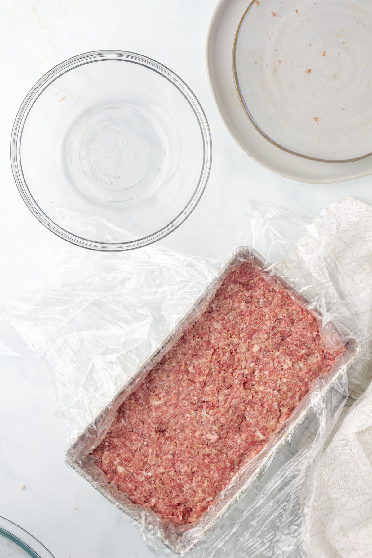 Raw square sausage mixture pressed into a loaf pan, lined with plastic wrap.