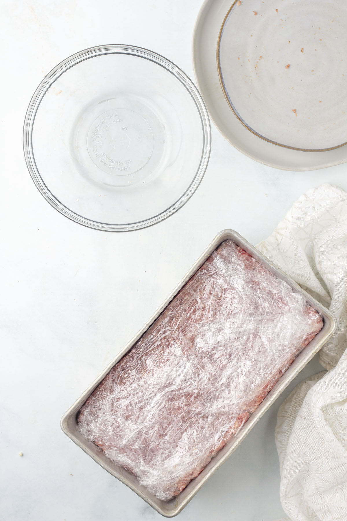 Raw square sausage mixture pressed into a loaf pan and covered with plastic wrap.