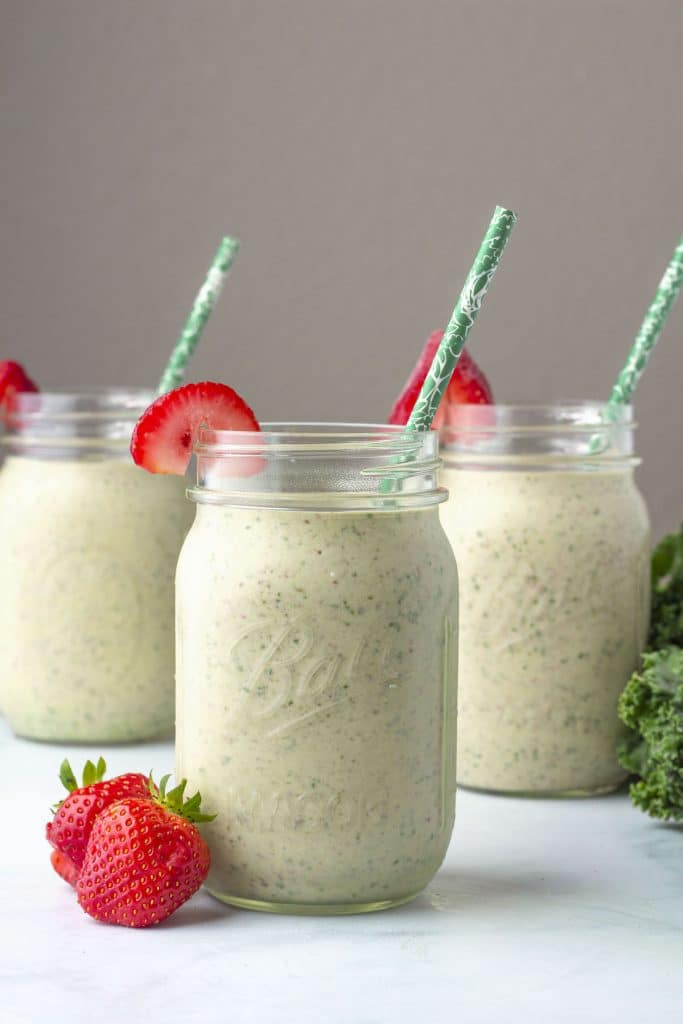 3 mason jars full of a light coloured smoothie with green straws.