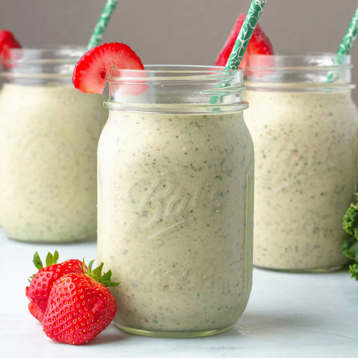 3 mason jars full of a green smoothie with straws and strawberries.
