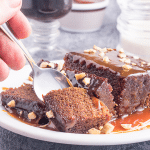A piece of sticky toffee pudding on a plate, smothered in toffee sauce.
