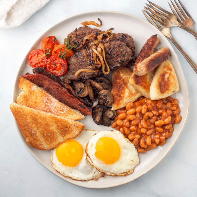 A plate of breakfast food with eggs, beans, Lorne sausage, Scottish potato scones, tomatoes, mushrooms, bacon, pork sausage links, and toast.