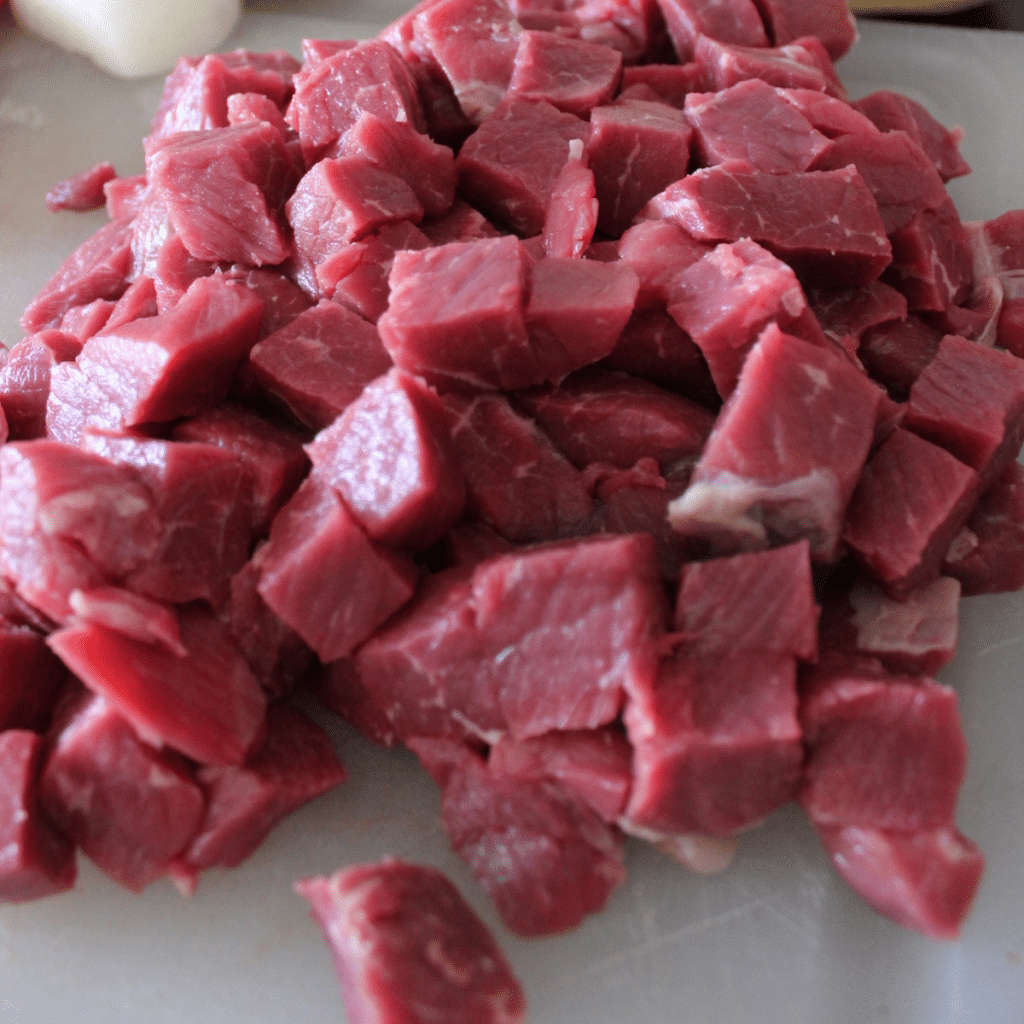 Raw beef cut into cubes on a plastic cutting board.