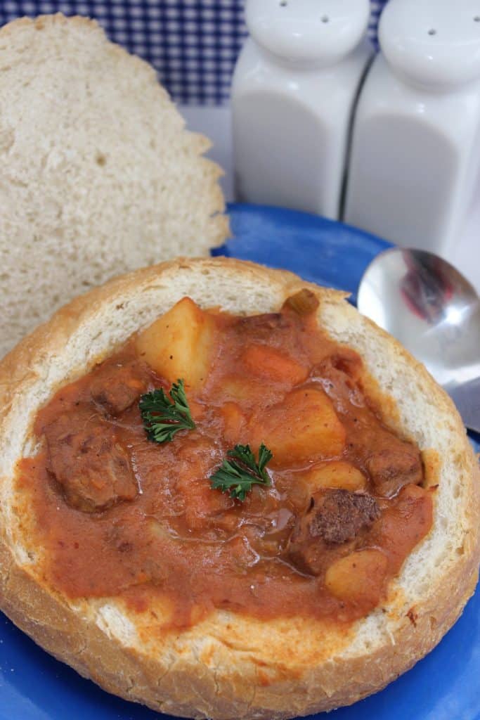 A bowl of stew in a bread bowl on a blue plate.